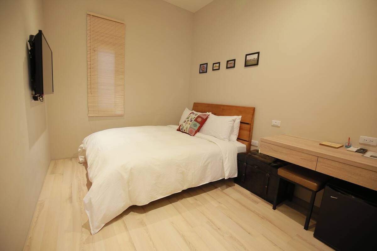 A bedroom with a bed, a desk, a bench, and a small refrigerator.