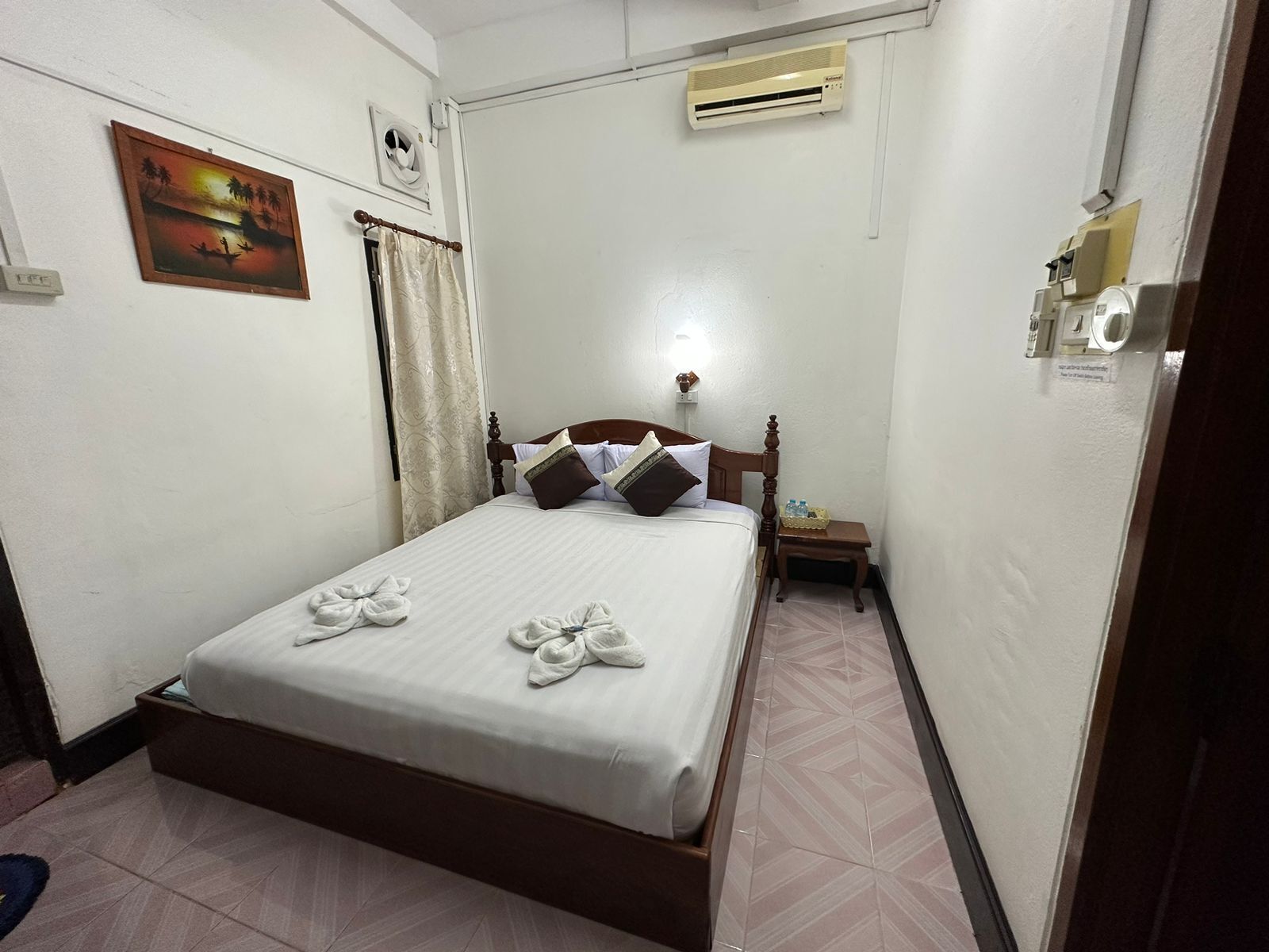 A neatly made bed with towels, a nightstand, a wall-mounted air conditioner, and a painting on the wall.