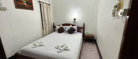 A neatly made bed with towels, a nightstand, a wall-mounted air conditioner, and a painting on the wall.