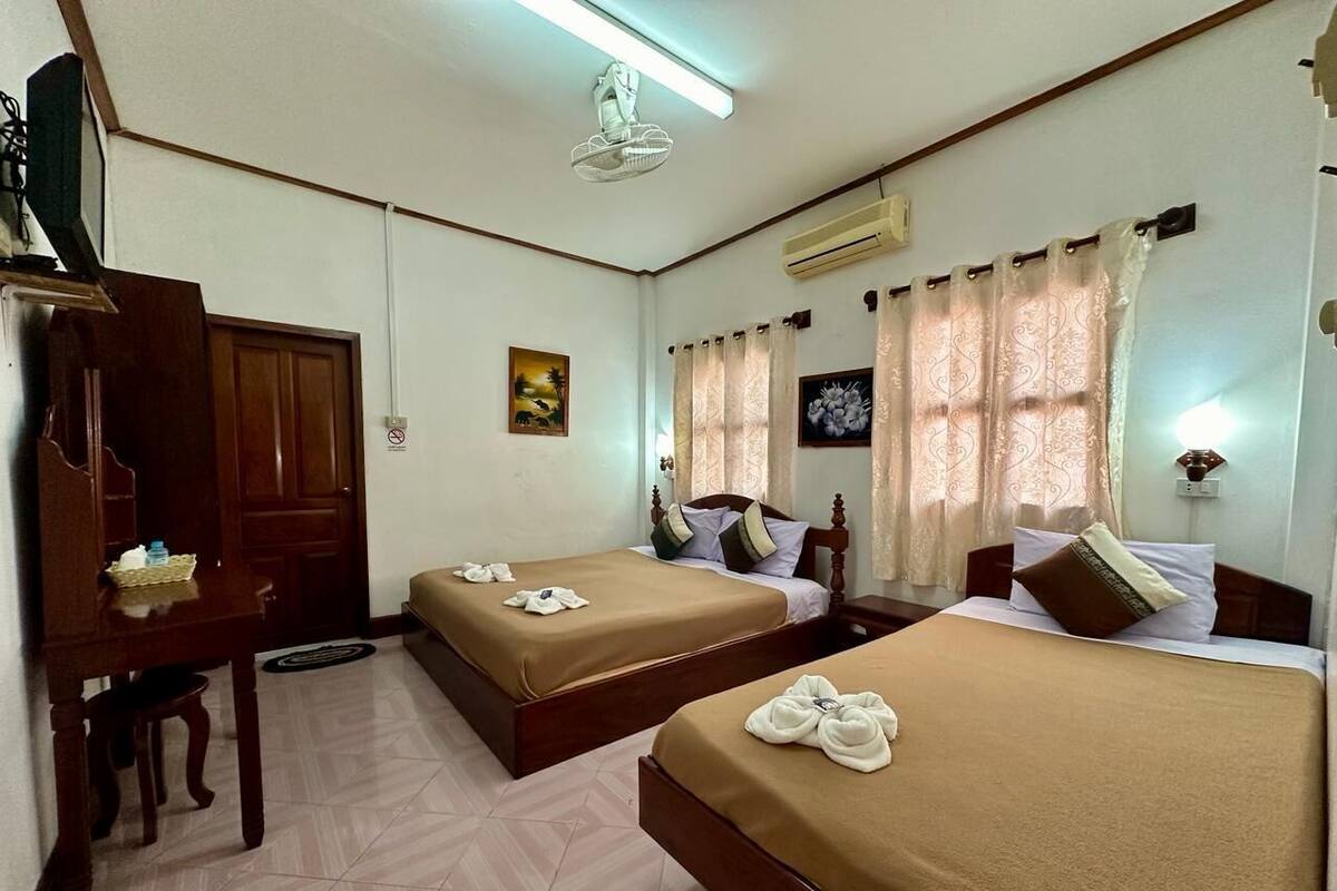 A hotel room with two beds, a desk, a chair, a television, and a ceiling fan.