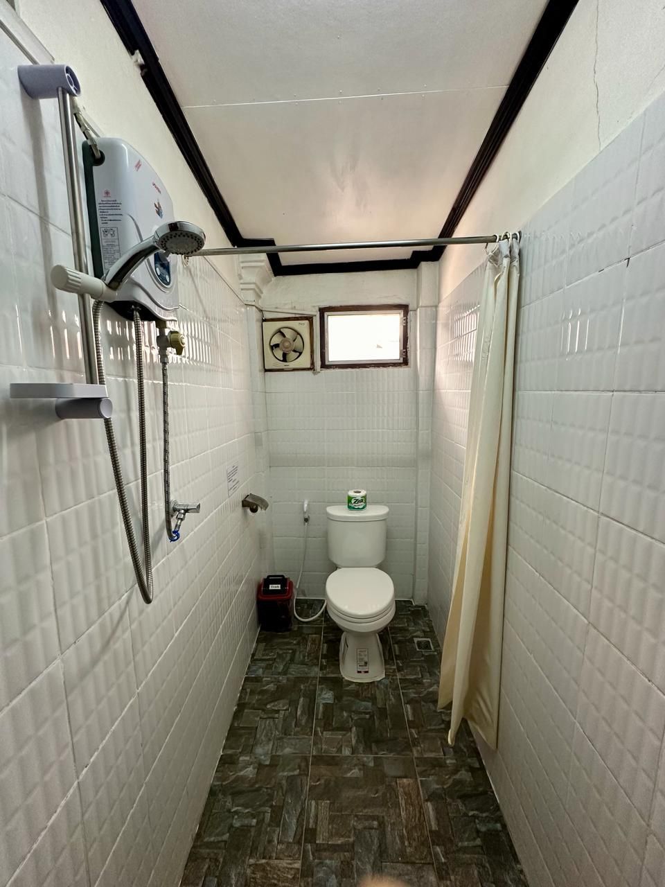 A narrow bathroom with a shower, toilet, and a small window.