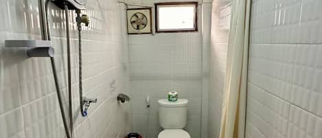 A narrow bathroom with a shower, toilet, and a small window.