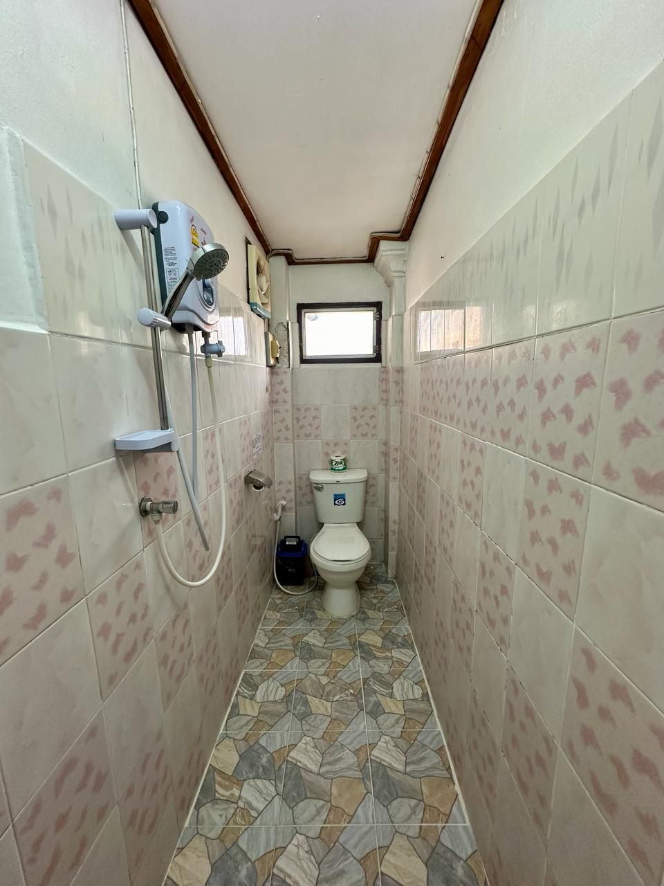 Un baño estrecho con ducha, inodoro y un pequeño ventanal.