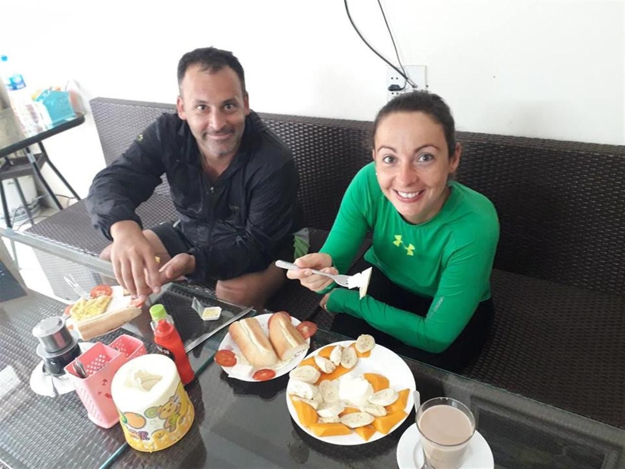 Two people seated at a table with food and drinks, a bottle, and a cup.