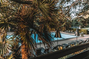 A pool area with lounge chairs and umbrellas, surrounded by palm trees. - Badhotel Rockanje & Brasserie Lodgers (Rockanje)