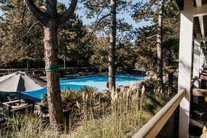 Ein Poolbereich, umgeben von hohen Bäumen, mit Liegestühlen und Sonnenschirmen.