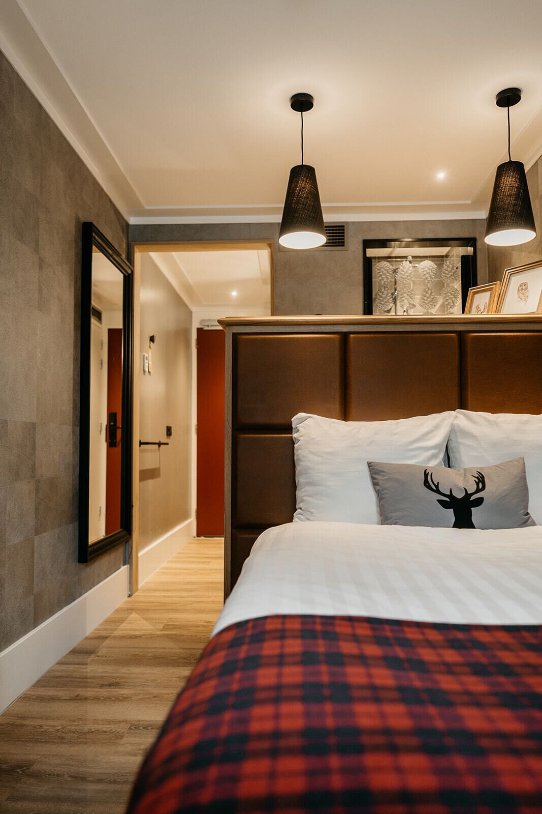 Een moderne slaapkamer met een groot bed, een hoofdbord met opbergruimte, een spiegel en twee hanglampen.