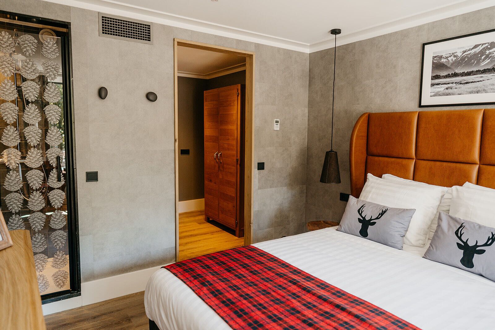 A bedroom with a large bed, a wooden wardrobe, a red plaid throw, and a framed picture on the wall.