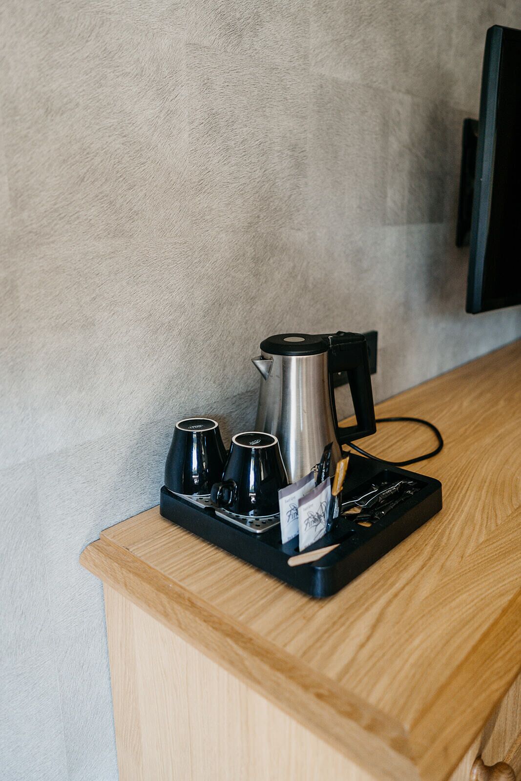 A coffee station with a coffee maker, cups, and a tray on a wooden counter.