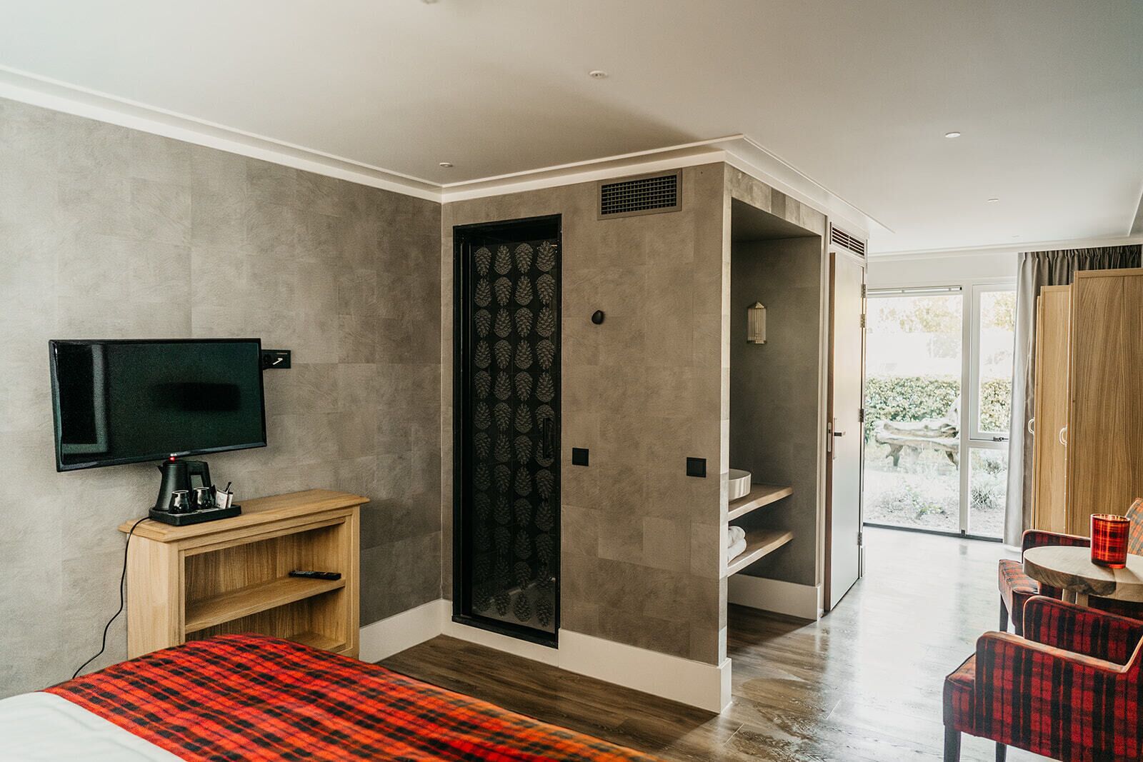 A modern bedroom with a TV, wooden bedside table, and a red plaid bedspread.
