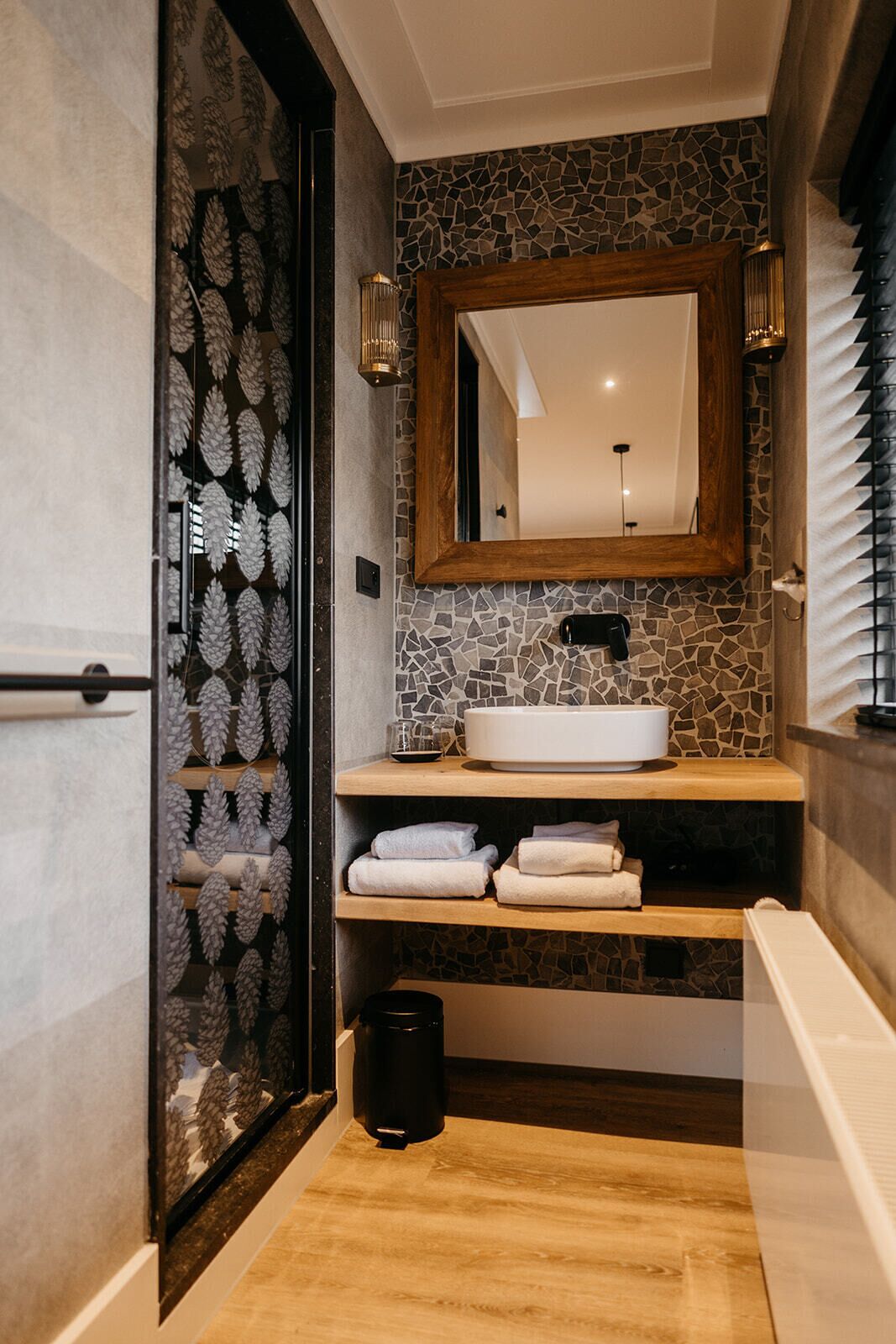 A modern bathroom with a stone backsplash, a wooden vanity, a large mirror, and a glass shower enclosure.