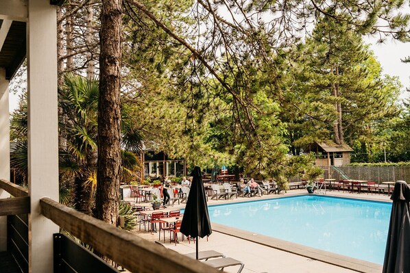 An outdoor pool area with lounge chairs and tables, surrounded by trees and a wooden structure. - Badhotel Rockanje & Brasserie Lodgers (Rockanje)