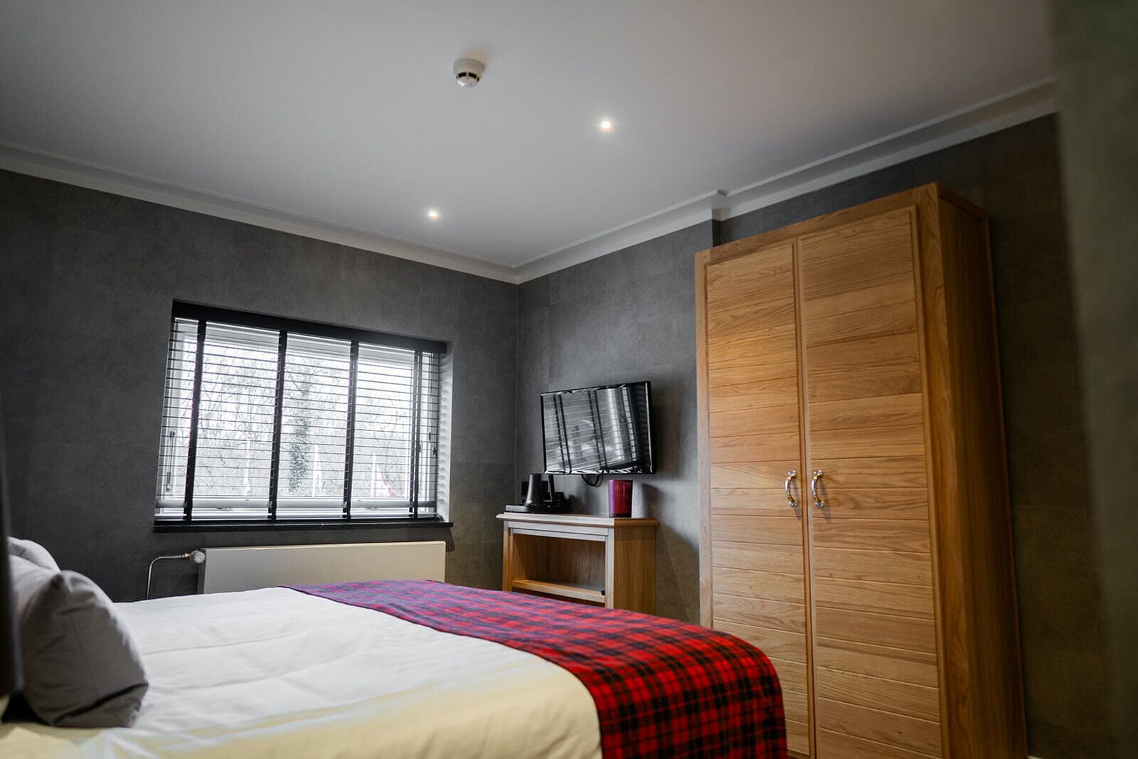 Un dormitorio con cama, armario, televisor y ventana con persianas.