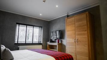 Un dormitorio con cama, armario, televisor y ventana con persianas.