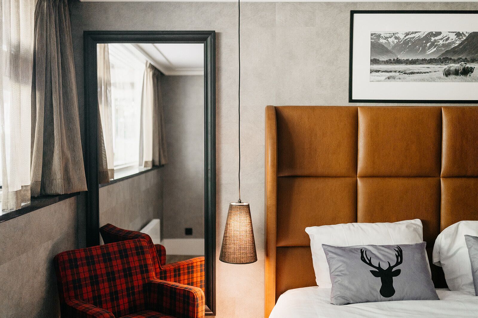 Habitación de hotel con una cama grande, un sillón rojo a cuadros, una lámpara y un cuadro en la pared.