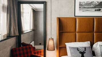 Habitación de hotel con una cama grande, un sillón rojo a cuadros, una lámpara y un cuadro en la pared.