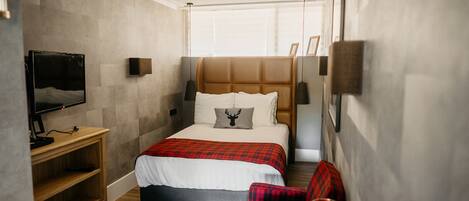 Une chambre d’hôtel avec un lit, une télévision, une étagère en bois, une couverture à carreaux rouges et une bougie rouge.