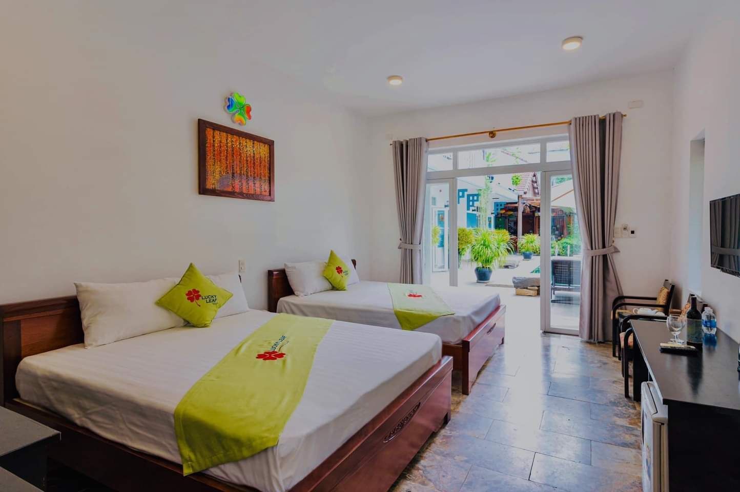 A hotel room with two beds, a desk, and a view of the outside.