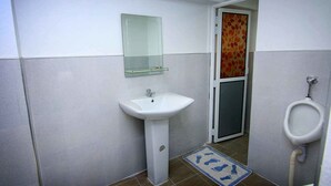 Ein Badezimmer mit Waschbecken, Spiegel, Urinal und Duschabtrennung.