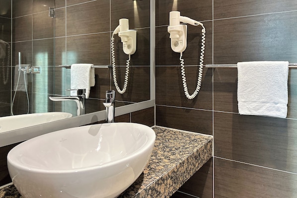 Un baño moderno con un lavamanos grande de color blanco, un espejo y dos secadores de pelo fijados en la pared.