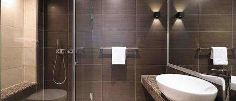 A modern bathroom with a glass-enclosed shower, a white sink, and dark tiled walls.