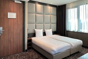 Habitación de hotel moderna con una cama grande, cabecera acolchada, un mapa enmarcado en la pared y vistas a la ciudad desde la ventana.