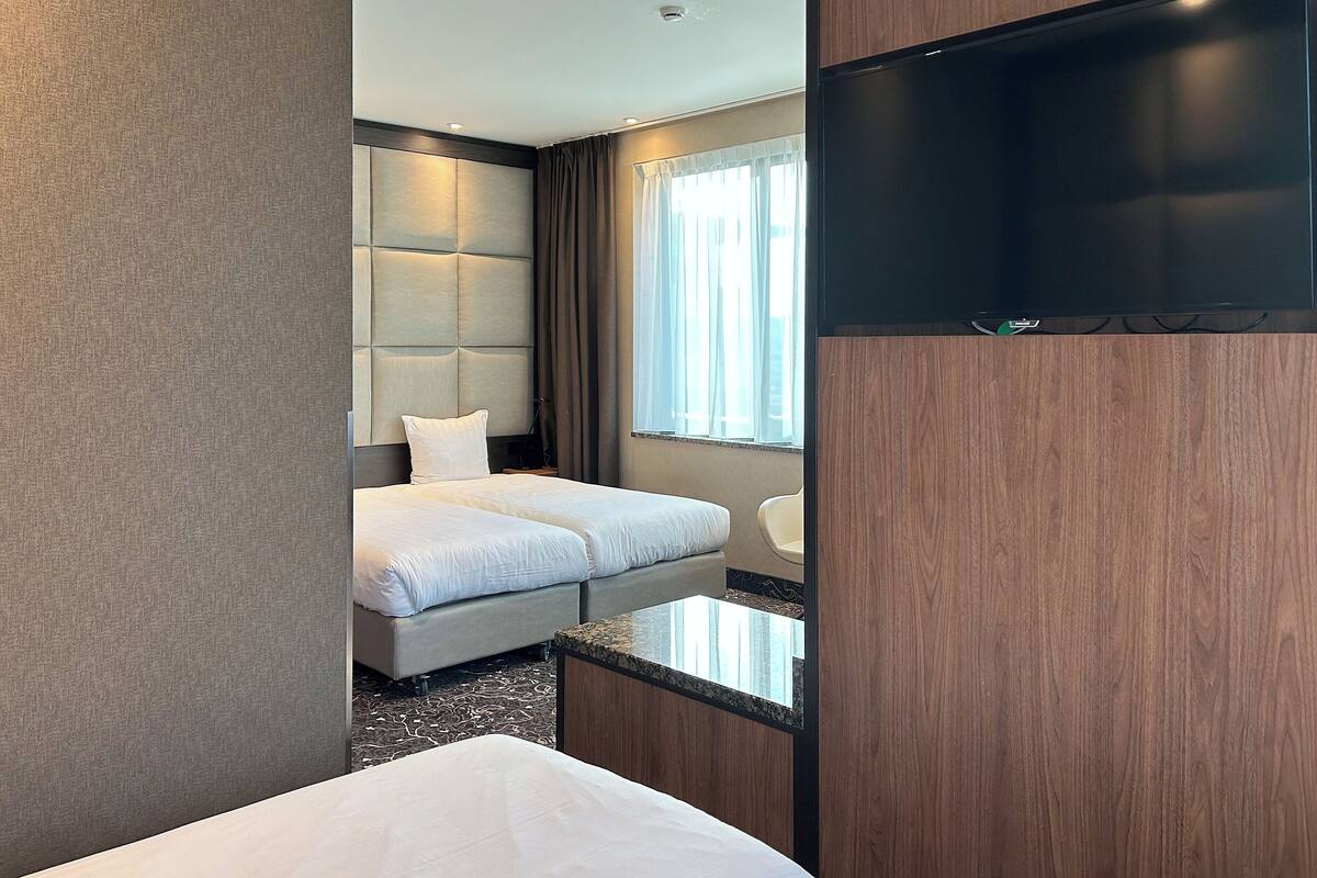 A modern hotel room with a bed, a TV, and a window with curtains.