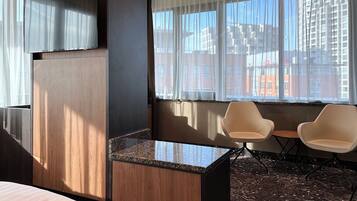 A hotel room with a bed, a small table, two chairs, a TV, and a window with a city view.