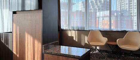 A hotel room with a bed, a small table, two chairs, a TV, and a window with a city view.