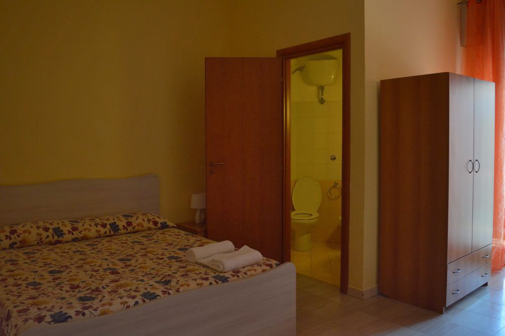 Un dormitorio con una cama, un armario de madera y un baño visible a través de una puerta abierta.