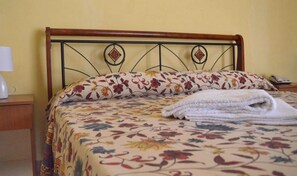 A bed with a floral bedspread and matching pillows, a wooden headboard, and a folded white towel on the bed.