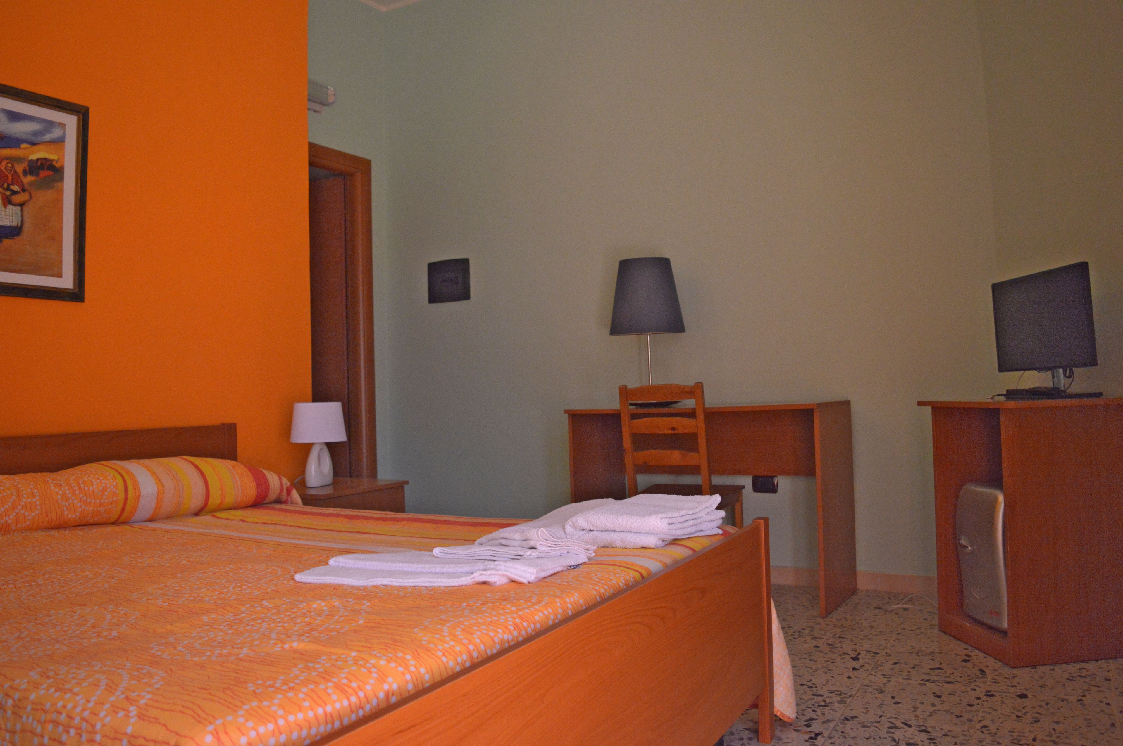 Habitación de hotel con cama, escritorio, silla, televisor y lámpara.