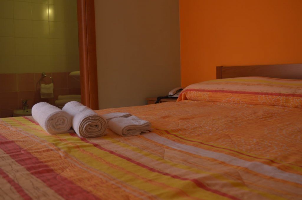 Habitación de hotel con cama, mesita de noche y baño visible a través de una puerta de cristal.