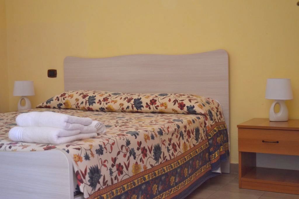 A bed with floral bedding, two bedside lamps, and a wooden nightstand with a drawer.