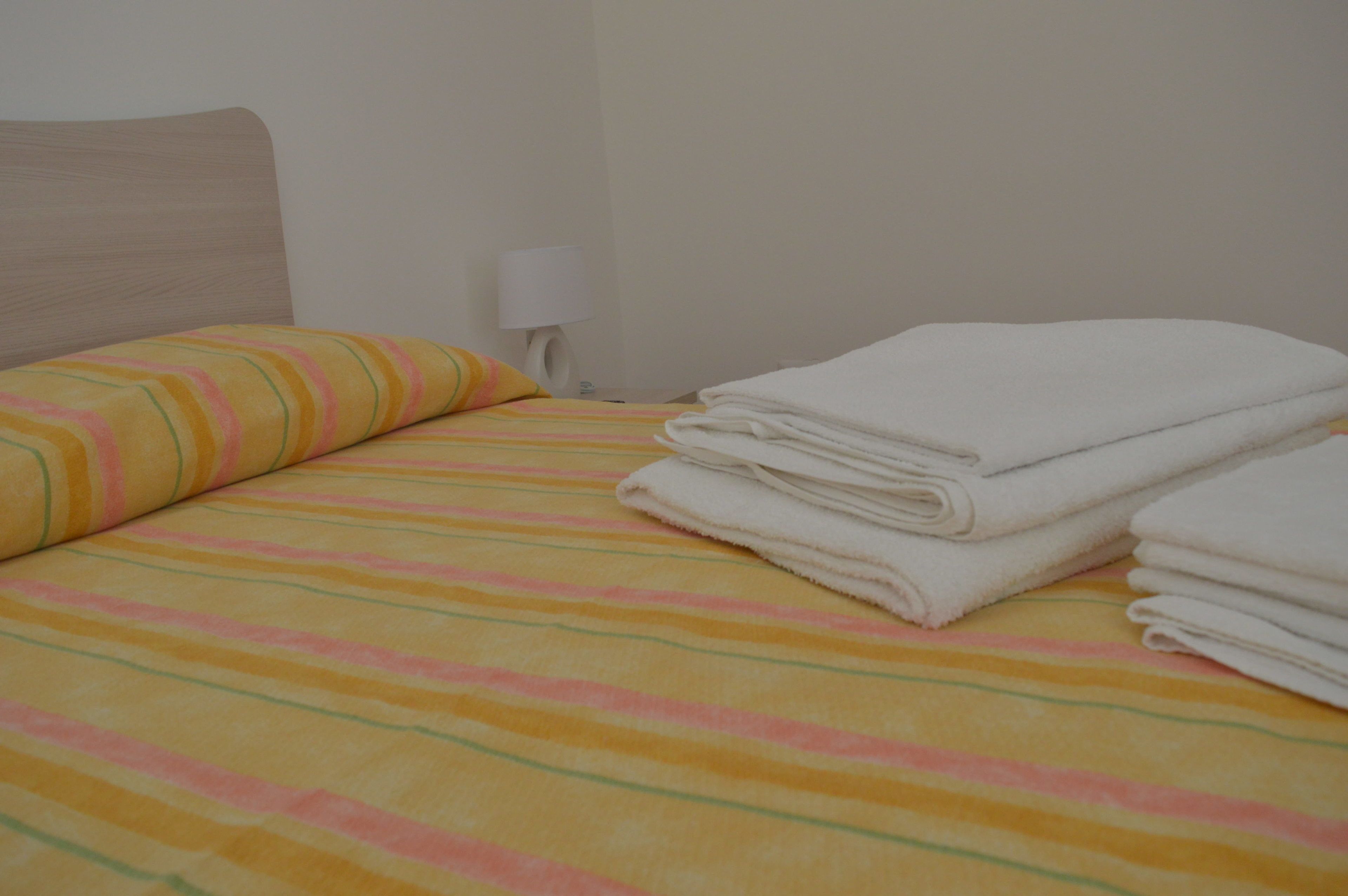 Una cama con ropa de cama a rayas, una almohada y toallas dobladas.