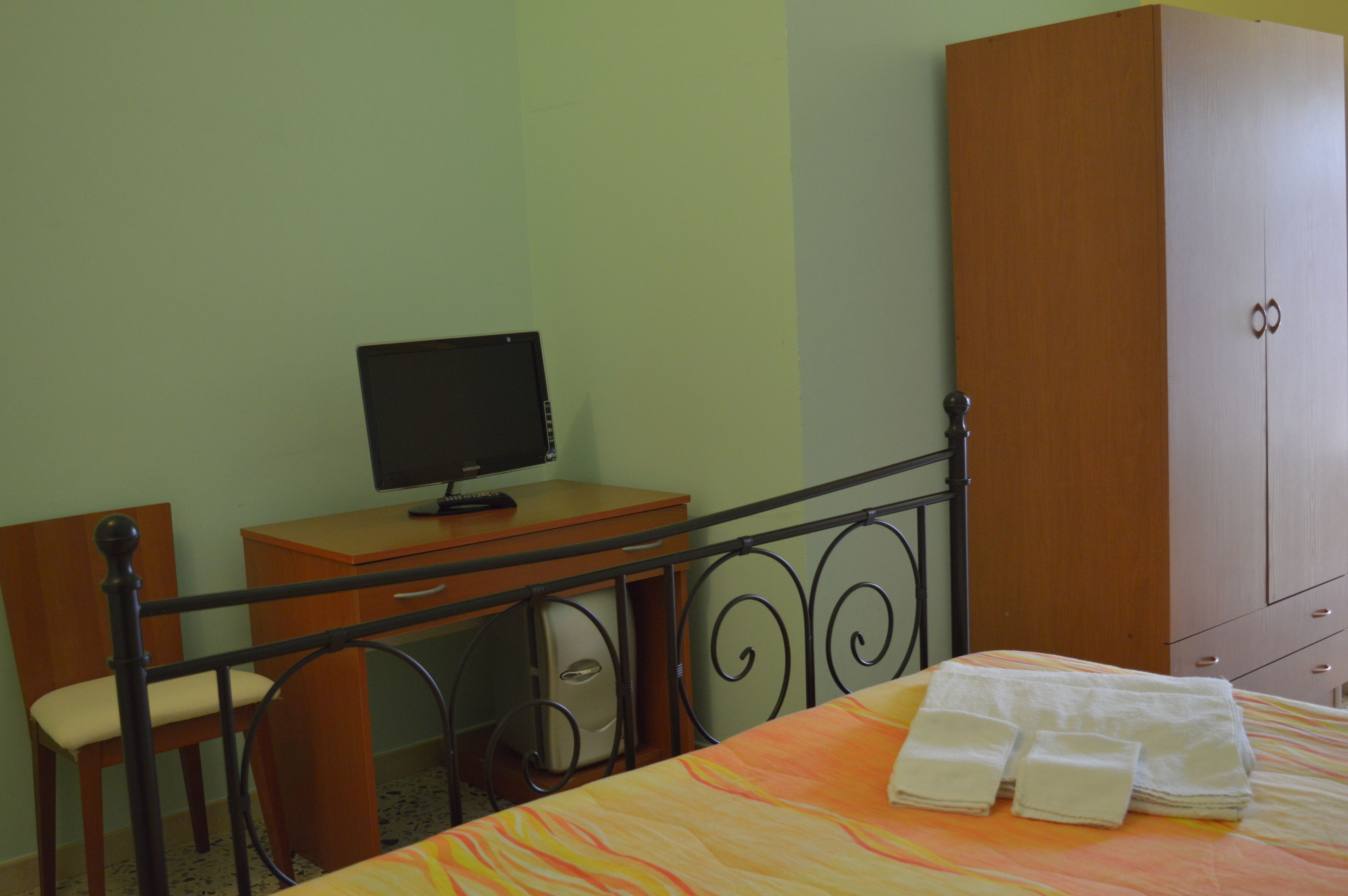 Una habitación con una cama, un escritorio con computadora, una silla y un armario.
