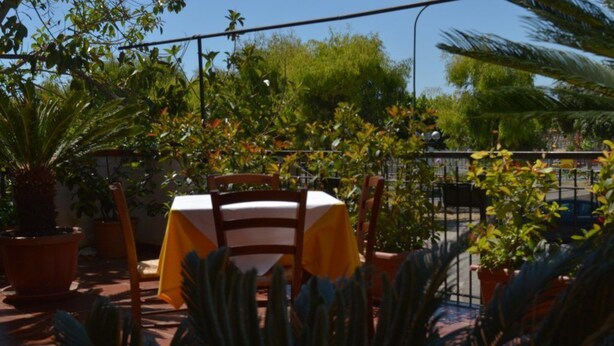 An outdoor patio with a table and chairs, surrounded by potted plants and a railing. - B&B Scalea Rooms (Scalea)