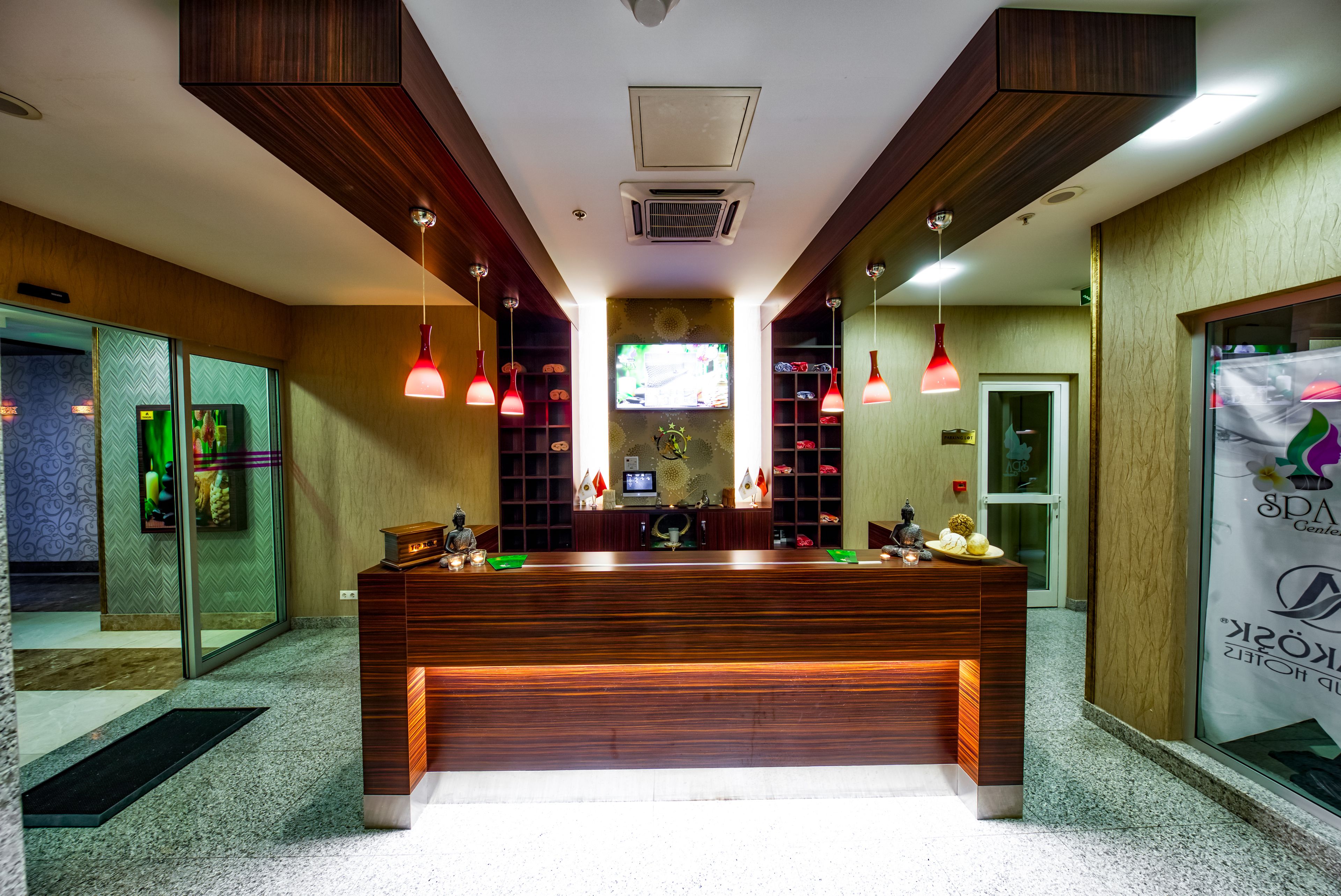 Una recepción con mostrador de madera, lámparas colgantes rojas y una pantalla de televisión en la parte superior.