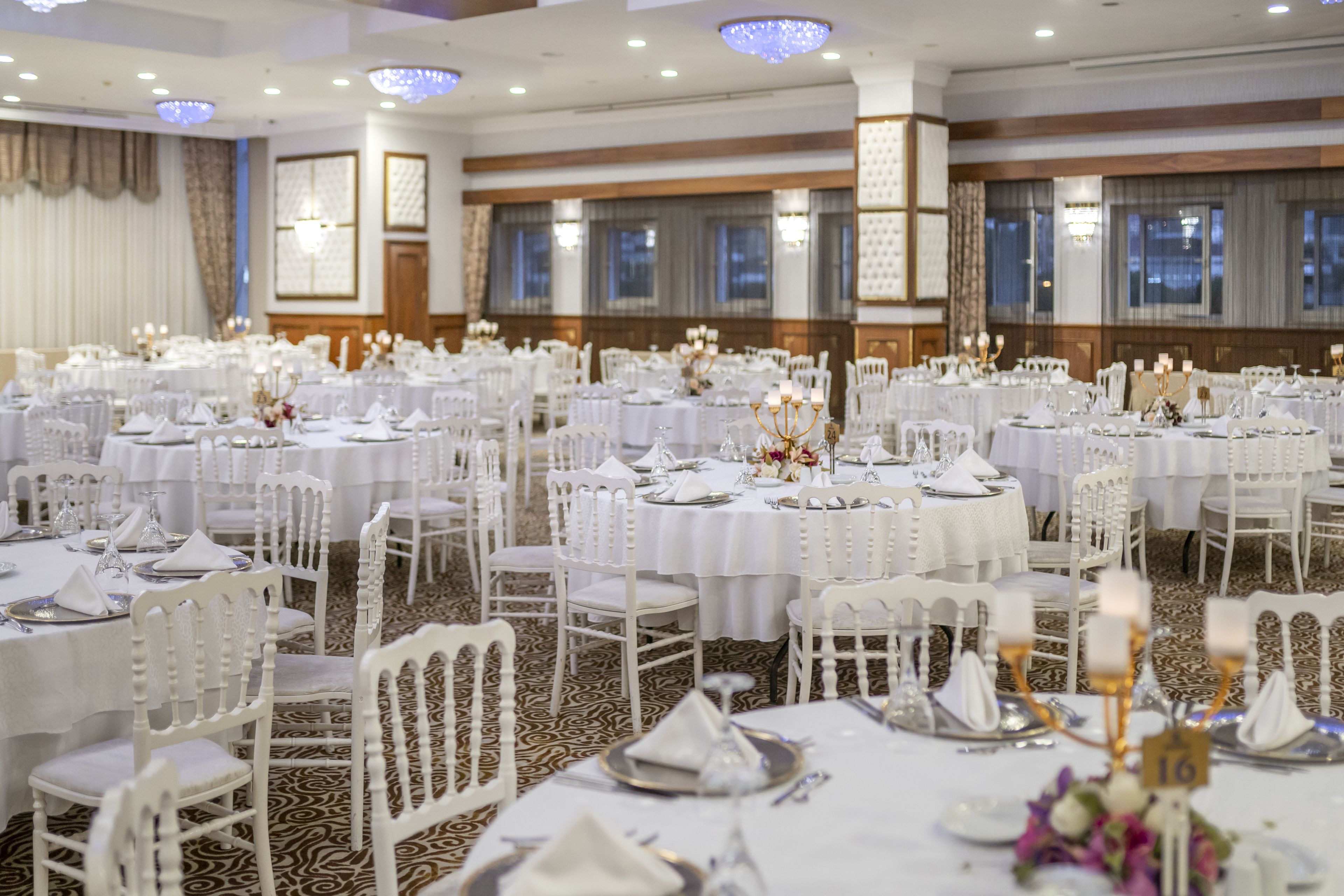 Un salón de banquetes con mesas redondas dispuestas para comer, sillas blancas y candelabros.