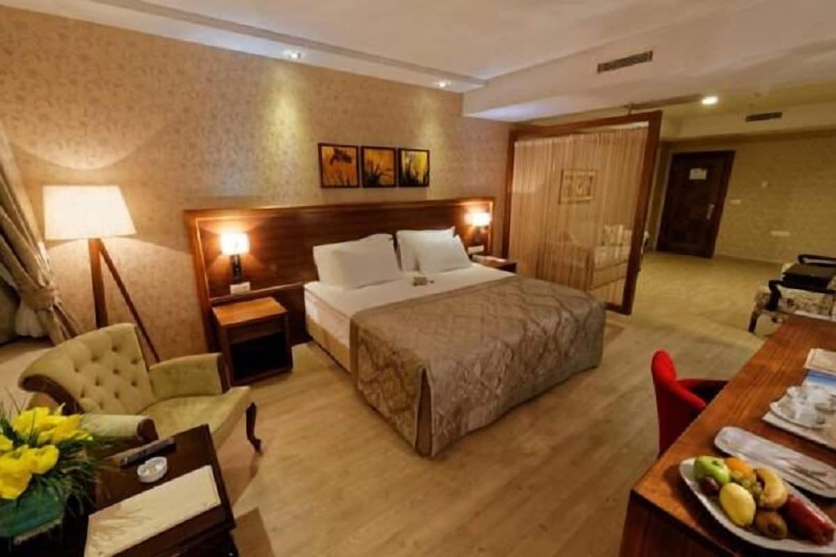 Habitación de hotel con cama, lámparas de noche, una silla, una mesa de comedor con fruta y vistas al pasillo.