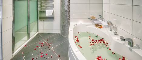 A modern bathroom with a glass-enclosed shower, a large bathtub with rose petals, and a tiled floor.