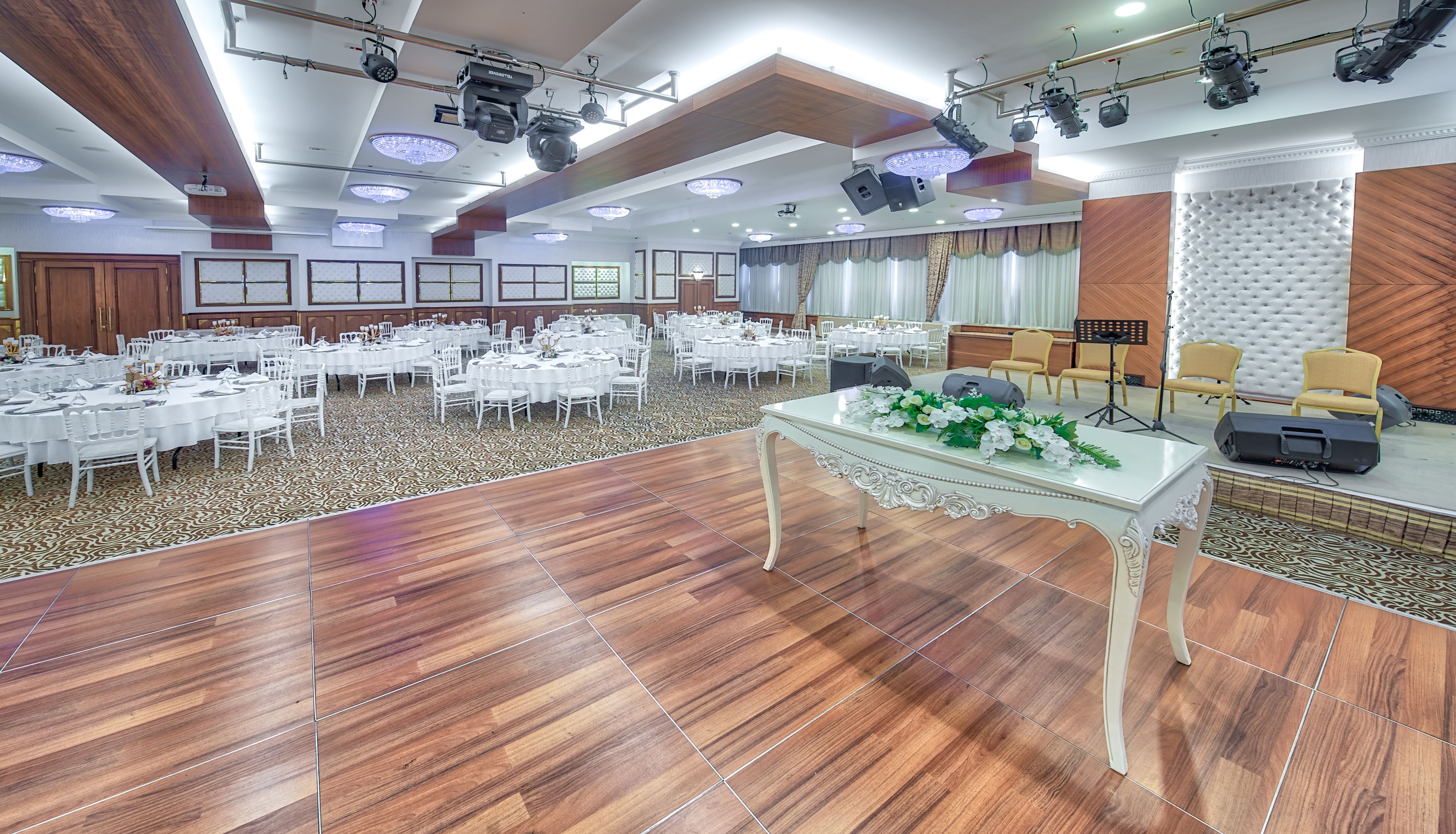 A banquet hall with round tables, white chairs, and a stage with musical equipment.