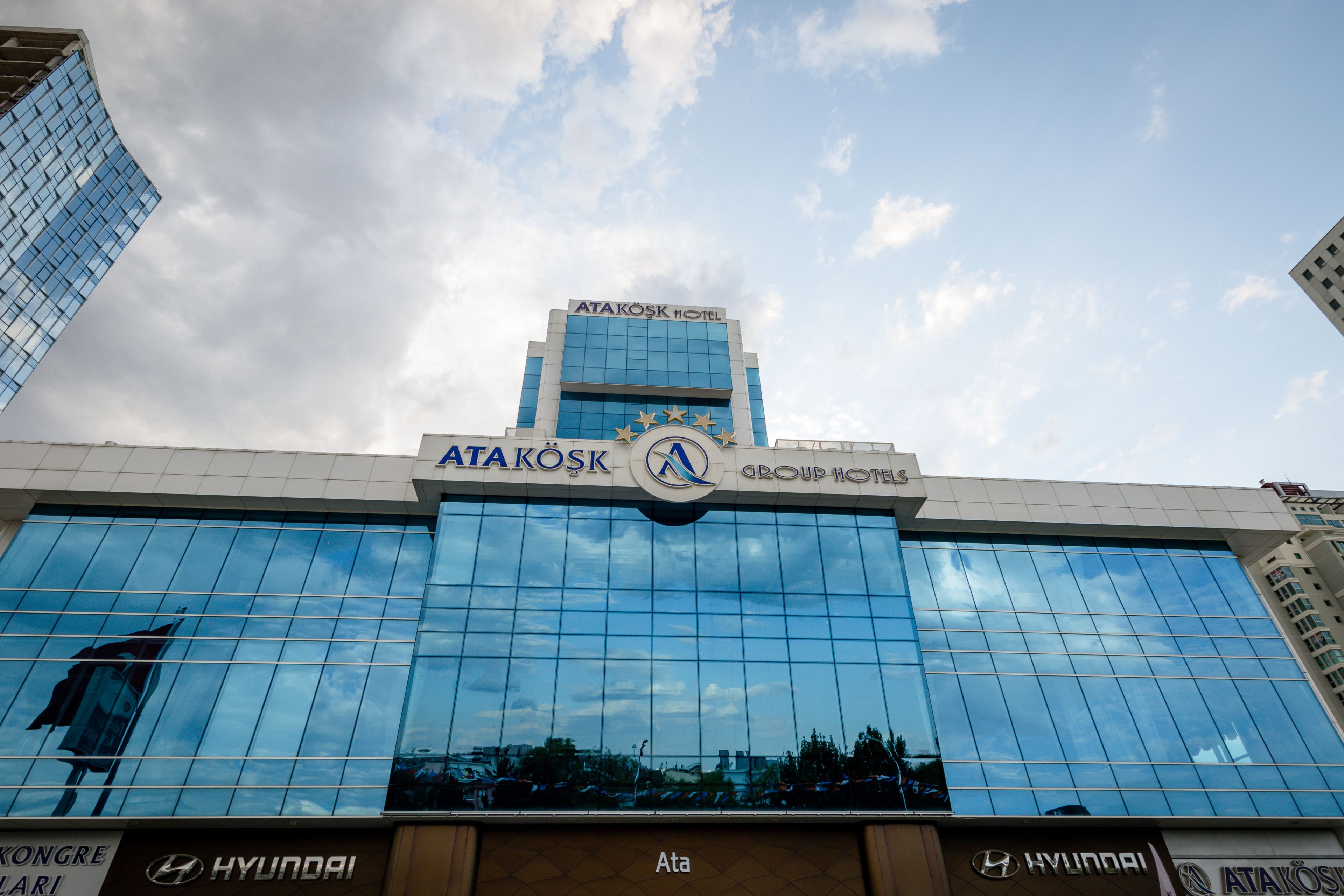 A modern hotel with a glass facade, branded with 'ATAKOSK HOTEL' and 'GROUP HOTEL' logos.