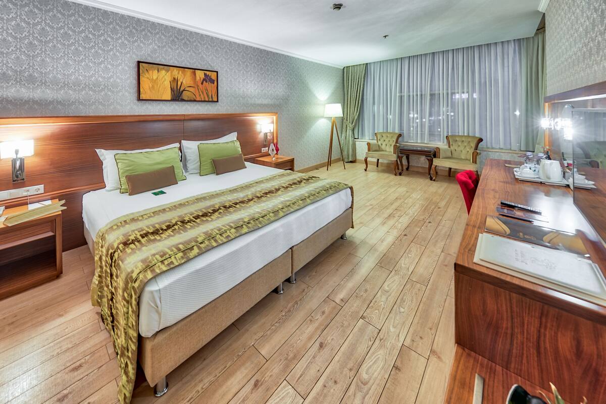 Habitación de hotel con una cama grande, cabecera de madera, mesitas de noche con lámparas, un escritorio con espejo y una silla.