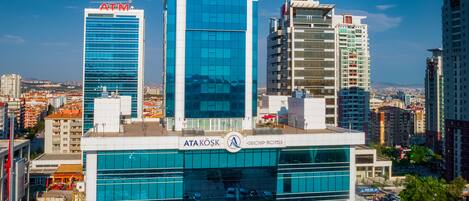 A modern hotel with a glass facade, ATAKOSK HOTEL branding, and a Hyundai dealership.