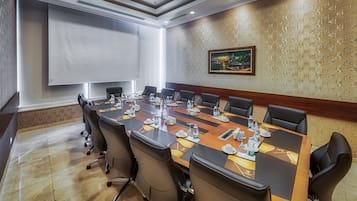 Ein Konferenzraum mit einem langen Tisch, mehreren Stühlen und einer Projektionsleinwand.