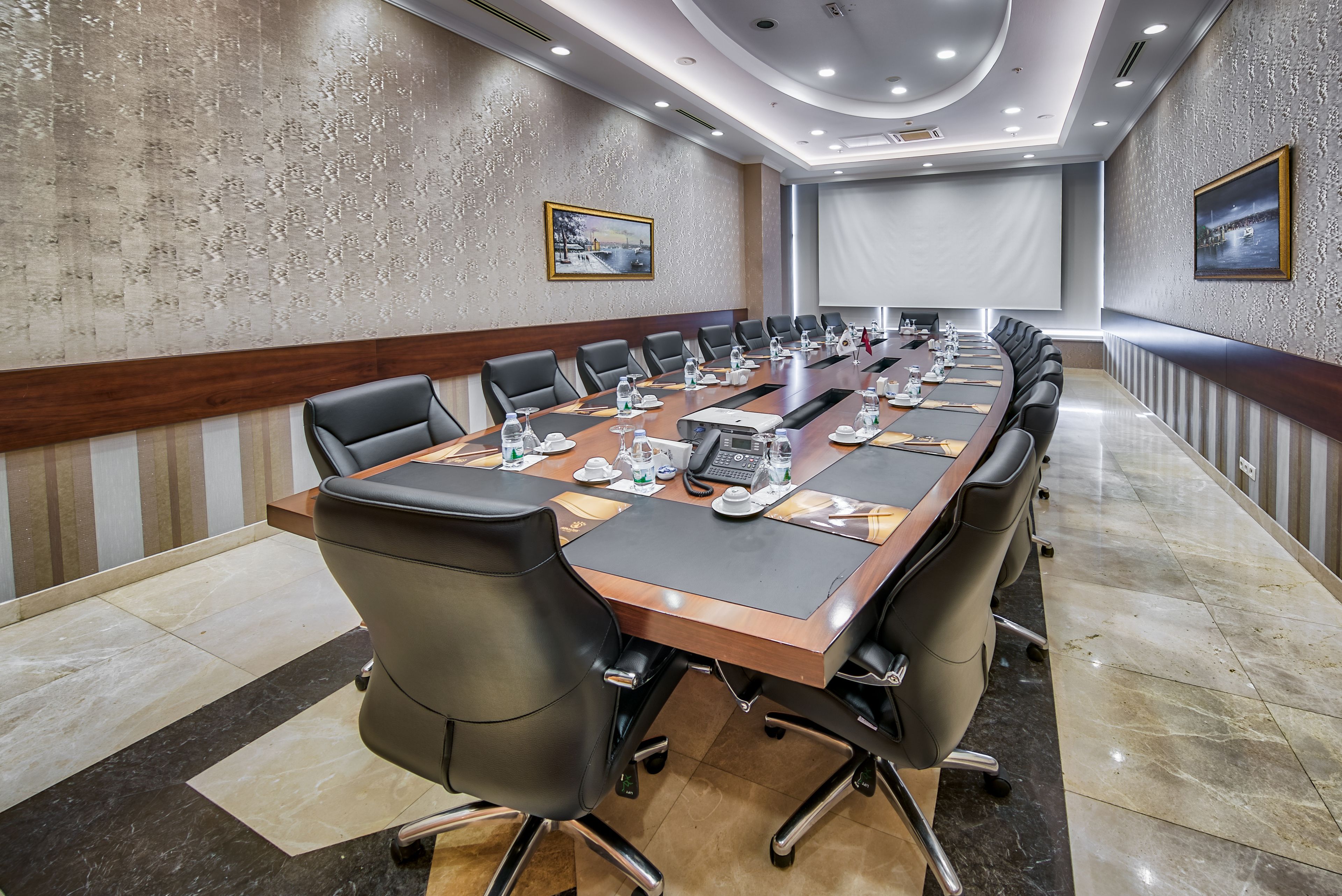A conference room with a long table, chairs, and a projector screen.