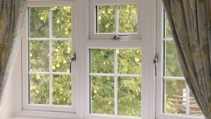 Ein Fenster mit weißen Rahmen und vielen Glasscheiben, teilweise zurückgezogene Vorhänge und Blick ins Grüne.