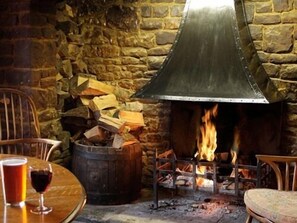 A stone wall with a metal fireplace, a wooden barrel, and a table with a glass of red wine. - The Anchor Inn (Bristol)