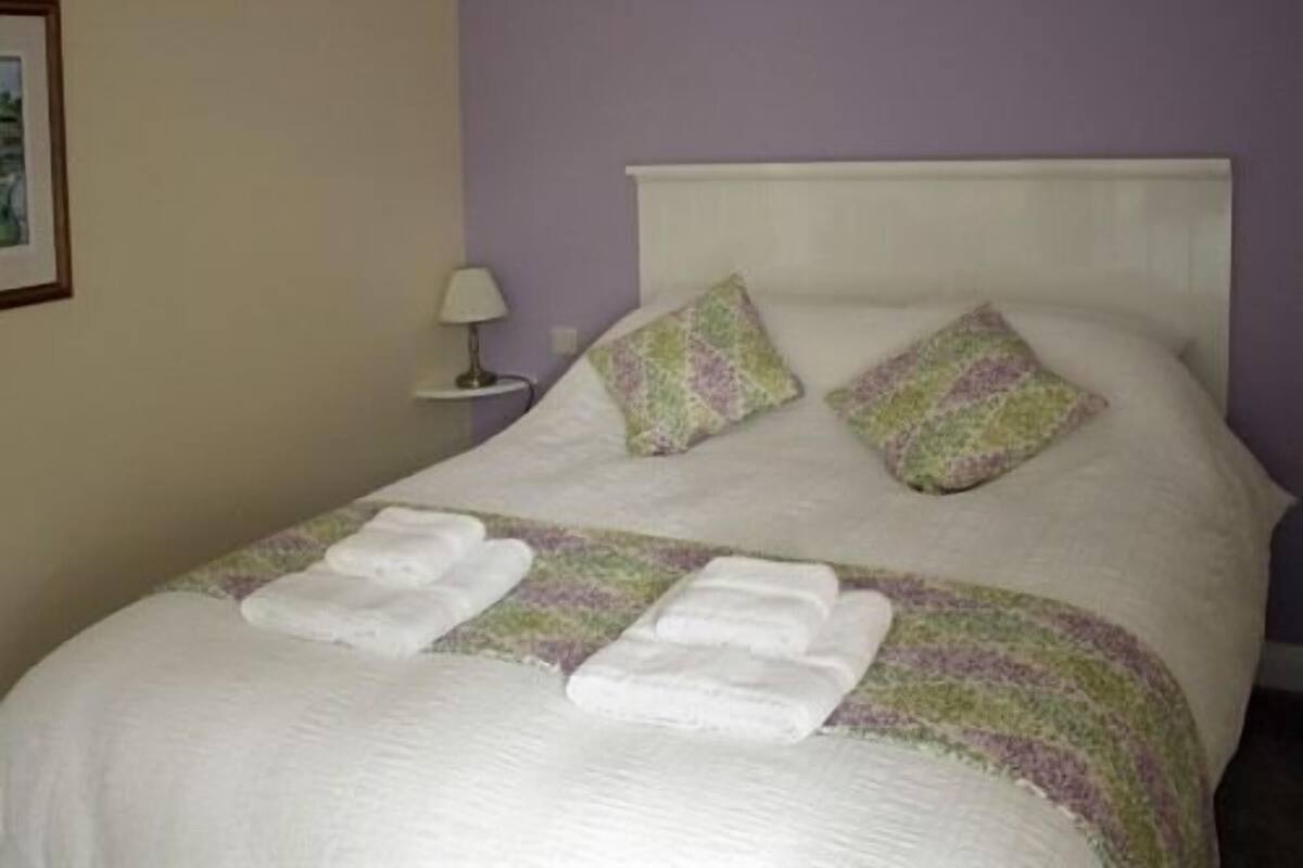 A neatly made bed with pillows and folded towels, a bedside lamp, and a framed picture on the wall.